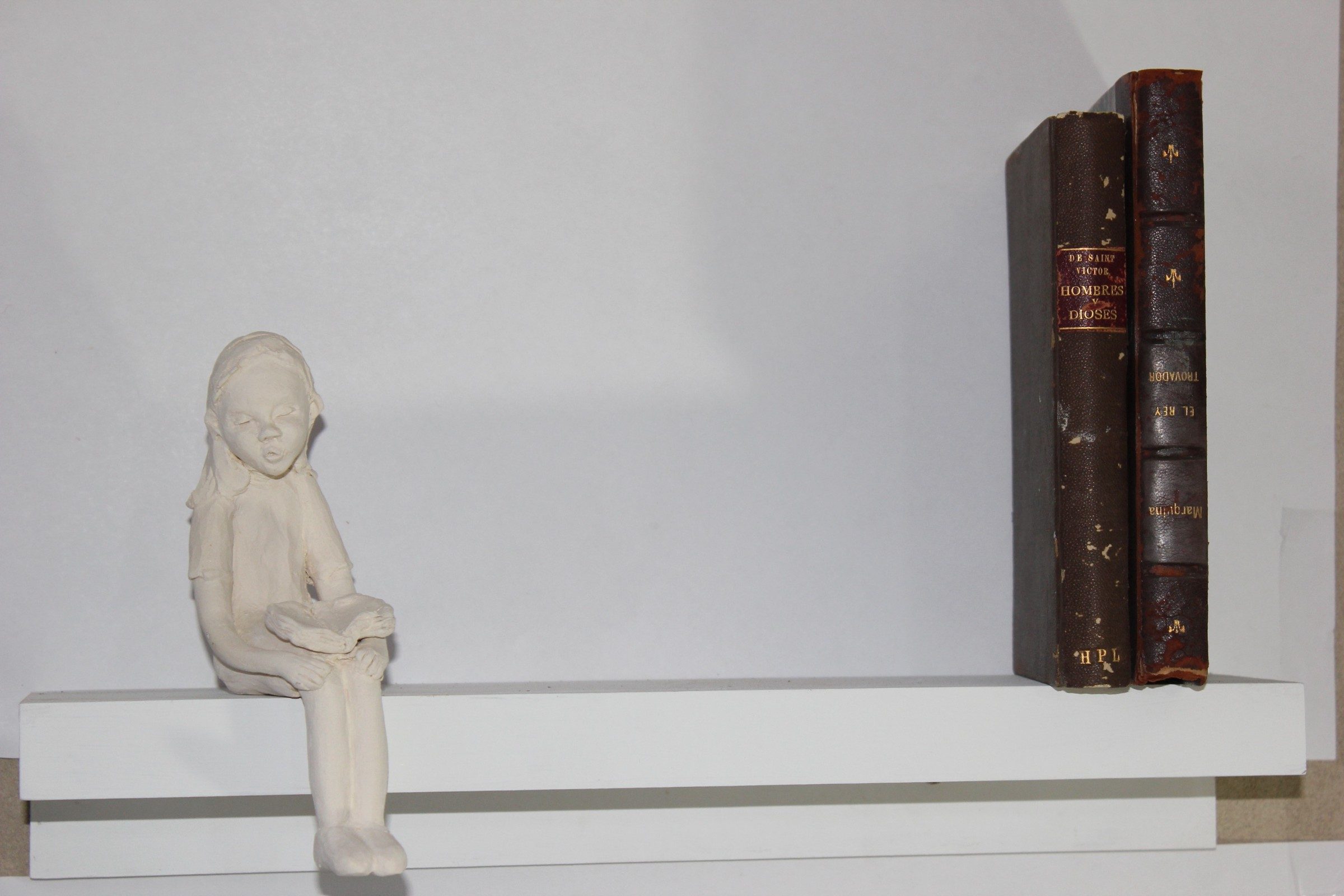 Niña de cerámica sentada en una repisa junto a dos libros antiguos